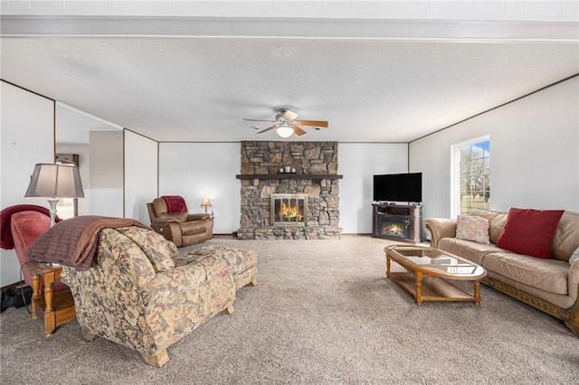 carpeted living area with ceiling fan, a stone fireplace, and a textured ceiling