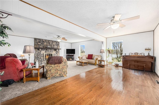 living area with ornamental molding, ceiling fan, a stone fireplace, a textured ceiling, and hardwood / wood-style flooring