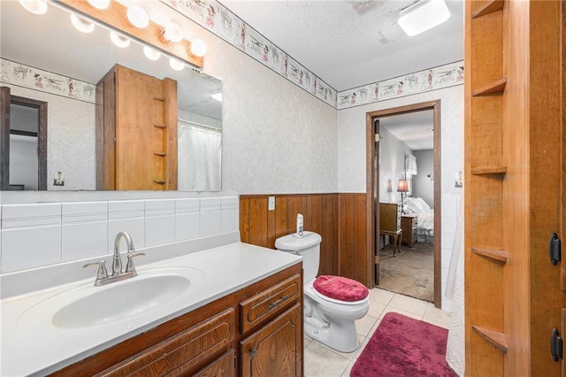 bathroom with a textured ceiling, toilet, vanity, wainscoting, and tile patterned floors