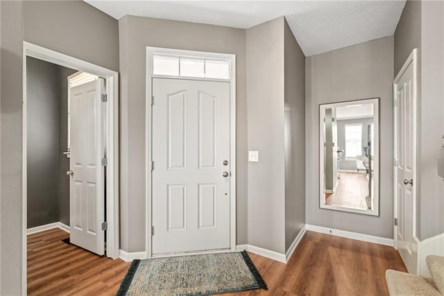 foyer entrance with stairway, a textured ceiling, baseboards, and wood finished floors