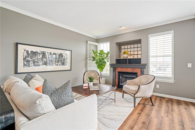 living area featuring a textured ceiling, wood finished floors, baseboards, ornamental molding, and a glass covered fireplace