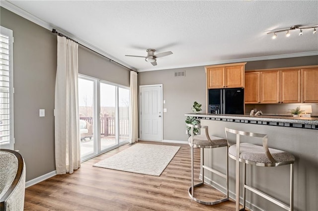 kitchen with light wood finished floors, visible vents, ornamental molding, a kitchen breakfast bar, and black refrigerator with ice dispenser