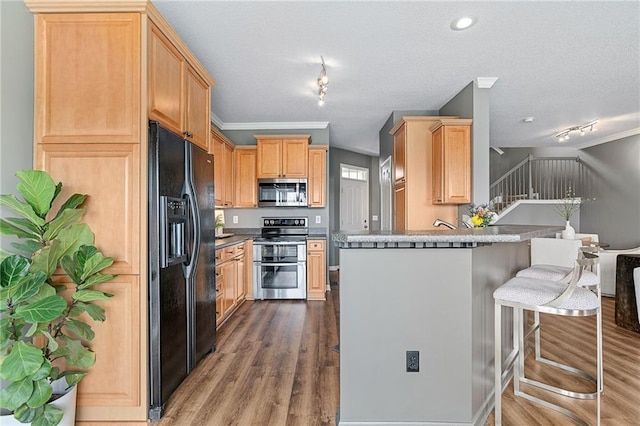 kitchen featuring a peninsula, a breakfast bar, wood finished floors, appliances with stainless steel finishes, and light brown cabinetry