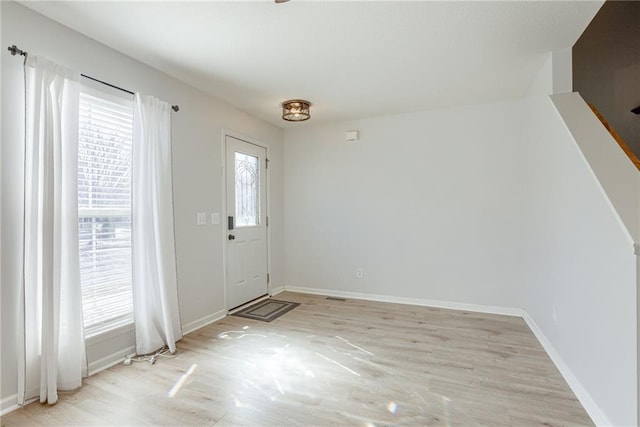 foyer with light wood-style floors, stairway, and baseboards