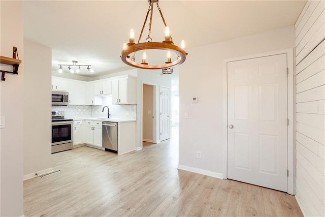 kitchen with stainless steel appliances, light countertops, backsplash, a sink, and light wood-type flooring