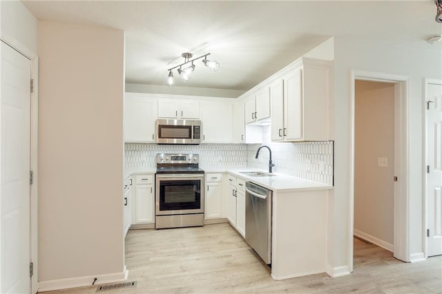 kitchen featuring backsplash, stainless steel appliances, a sink, and light wood finished floors