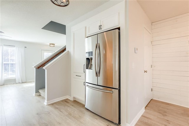 kitchen with wooden walls, light wood-type flooring, white cabinets, and stainless steel refrigerator with ice dispenser