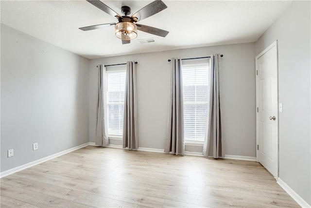 empty room with baseboards, light wood finished floors, visible vents, and a healthy amount of sunlight