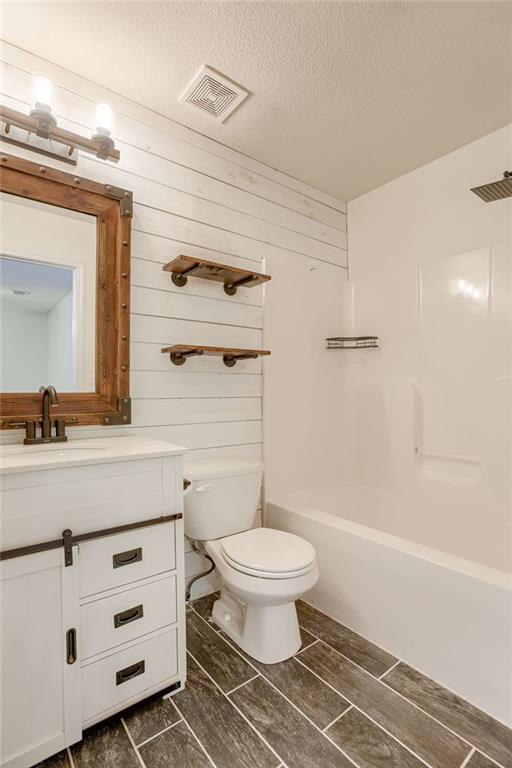 bathroom featuring visible vents, toilet, a textured ceiling, vanity, and shower / washtub combination