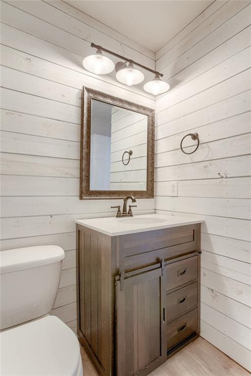 half bathroom featuring toilet, wood walls, wood finished floors, and vanity