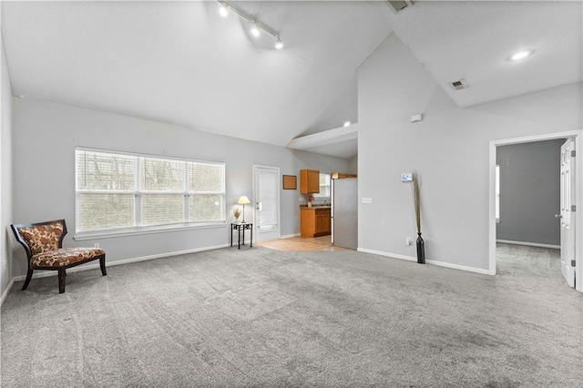 interior space with high vaulted ceiling, light colored carpet, visible vents, baseboards, and rail lighting