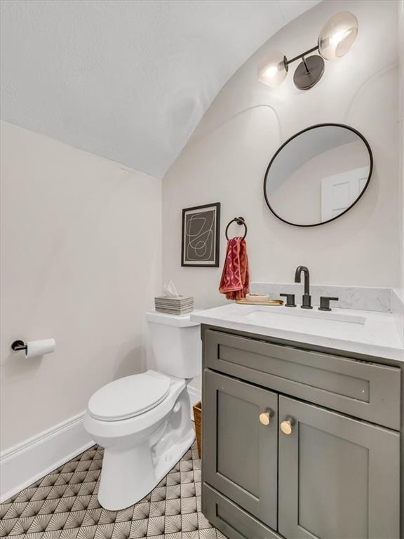 bathroom featuring toilet, vaulted ceiling, vanity, tile patterned flooring, and baseboards