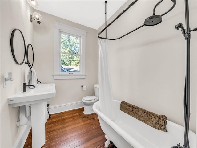 full bathroom with baseboards, toilet, hardwood / wood-style floors, curtained shower, and a freestanding tub