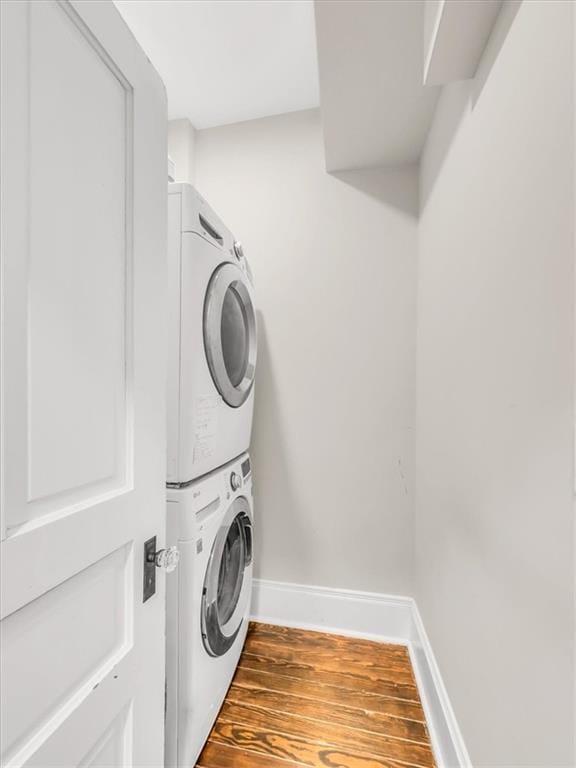 laundry room with stacked washer and dryer, laundry area, baseboards, and wood finished floors