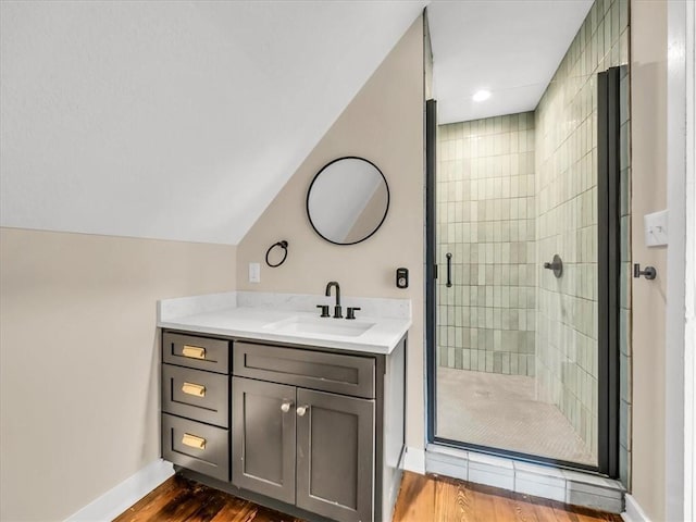 full bathroom featuring wood finished floors, vanity, baseboards, vaulted ceiling, and a shower stall