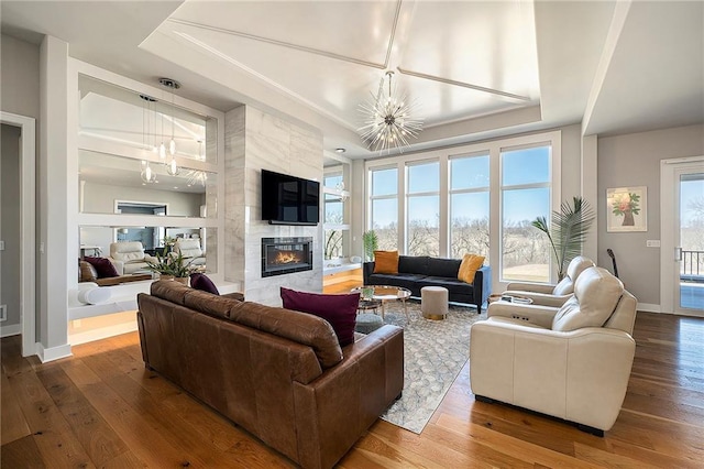 living area with baseboards, a tray ceiling, a premium fireplace, hardwood / wood-style flooring, and a notable chandelier