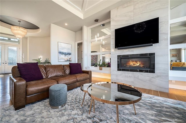 living room with french doors, a notable chandelier, wood finished floors, and a high end fireplace