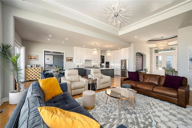 living area with a chandelier, light wood finished floors, and a raised ceiling