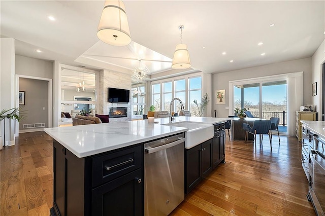 kitchen featuring a sink, a large fireplace, wood-type flooring, light countertops, and dishwasher