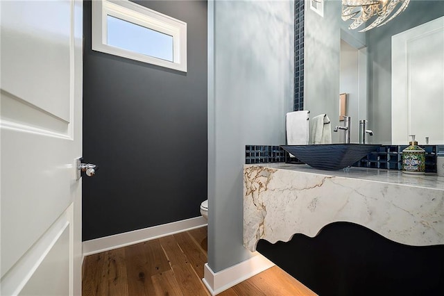 half bath featuring a sink, toilet, baseboards, and wood finished floors