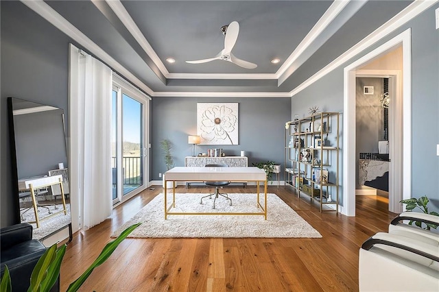 home office with a ceiling fan, a raised ceiling, crown molding, and wood finished floors