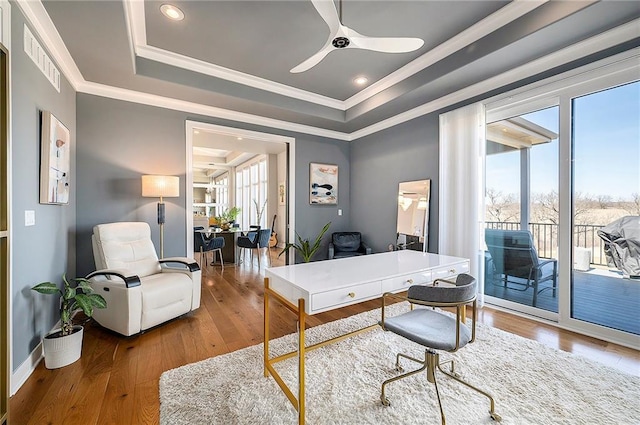 office area with crown molding, baseboards, a tray ceiling, a ceiling fan, and wood-type flooring