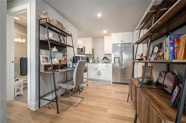 kitchen with a textured ceiling, light wood-style flooring, white cabinets, and stainless steel appliances