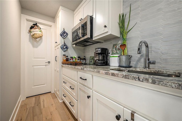 kitchen with a sink, decorative backsplash, white cabinets, stainless steel microwave, and light wood-type flooring