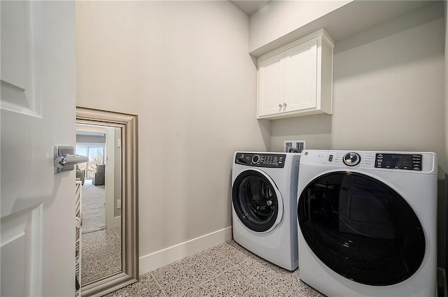 clothes washing area featuring washing machine and dryer, cabinet space, and baseboards