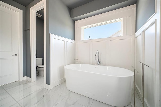 full bath with a decorative wall, marble finish floor, toilet, and a freestanding tub