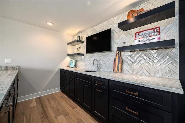 bar featuring a sink, decorative backsplash, baseboards, and wood finished floors