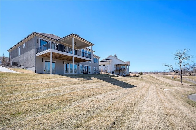 back of property with a balcony, cooling unit, a ceiling fan, stucco siding, and a lawn