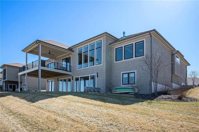 rear view of property featuring stucco siding, a yard, and a ceiling fan