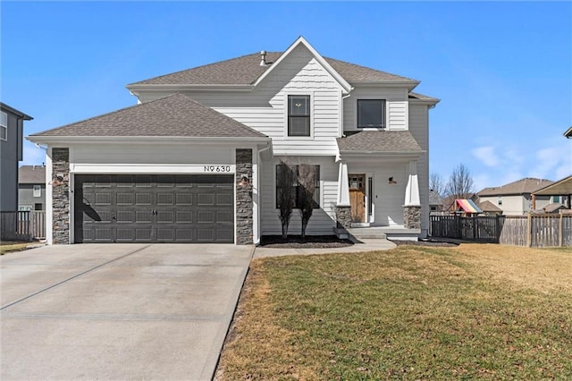 traditional-style home featuring concrete driveway, roof with shingles, an attached garage, fence, and a front lawn