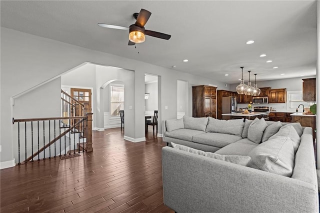 living room with recessed lighting, dark wood finished floors, arched walkways, and stairs