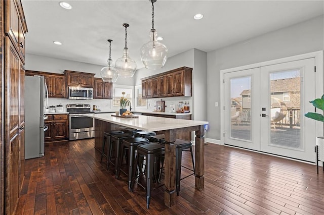 kitchen with dark wood-style floors, appliances with stainless steel finishes, light countertops, french doors, and a kitchen bar