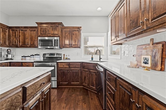 kitchen with appliances with stainless steel finishes, dark wood finished floors, a sink, and backsplash