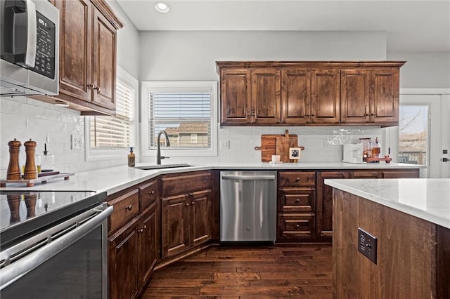 kitchen with stainless steel appliances, a sink, light countertops, backsplash, and dark wood-style floors