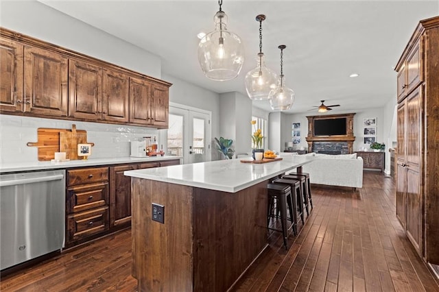 kitchen featuring decorative backsplash, dishwasher, dark wood-style flooring, light countertops, and a stone fireplace