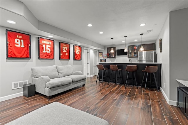 living area featuring baseboards, wet bar, visible vents, and wood finish floors