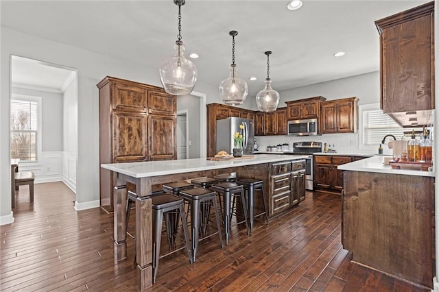 kitchen featuring wainscoting, a kitchen island, dark wood-type flooring, light countertops, and appliances with stainless steel finishes