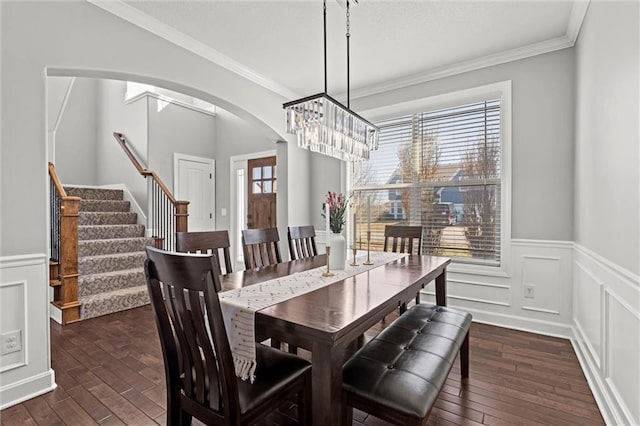 dining room featuring crown molding, dark wood-type flooring, a wainscoted wall, arched walkways, and a notable chandelier