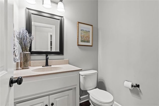 half bath with vanity, baseboards, and toilet
