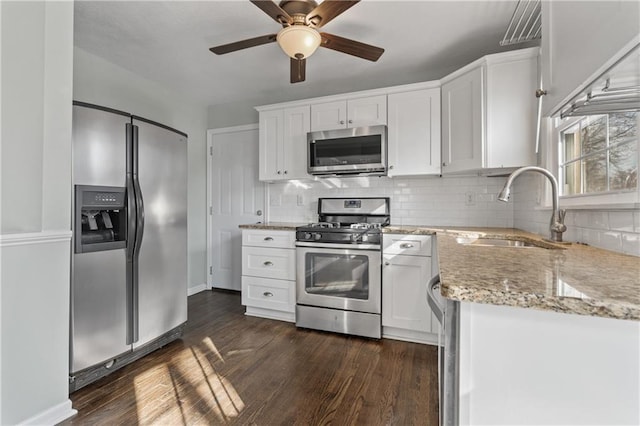 kitchen with a sink, dark wood finished floors, white cabinetry, appliances with stainless steel finishes, and light stone countertops