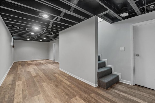 finished below grade area featuring stairway, baseboards, and wood finished floors