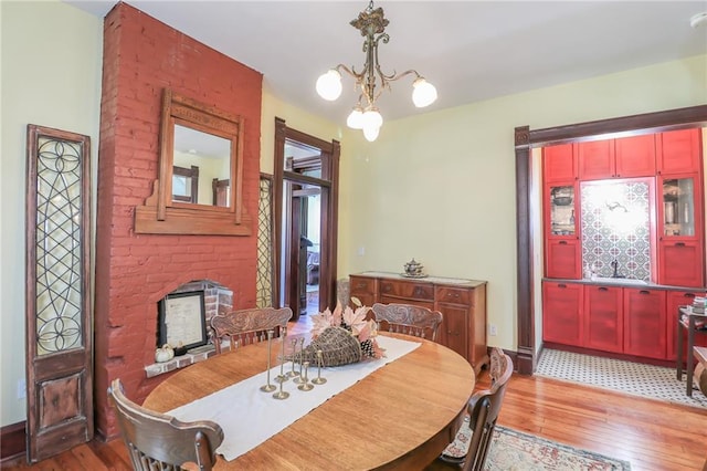 dining room with light wood finished floors, a fireplace, baseboards, and a notable chandelier