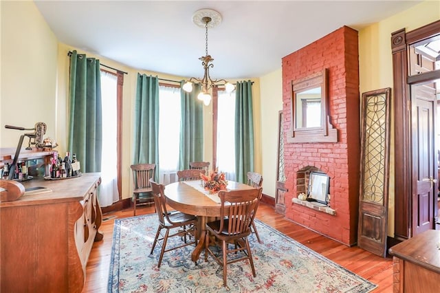 dining space with light wood-style floors, baseboards, a brick fireplace, and a chandelier