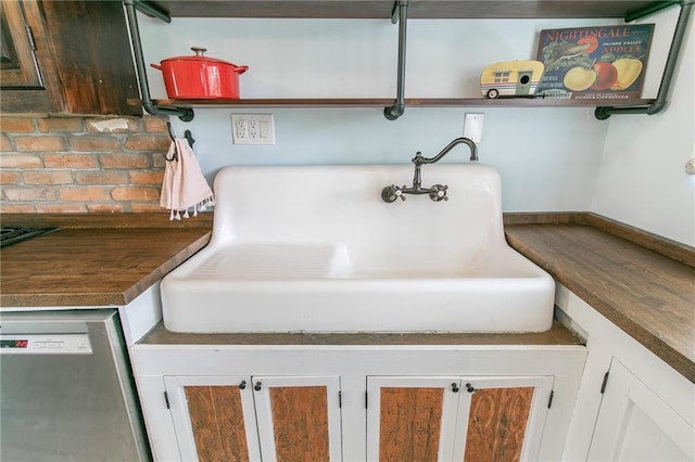 interior details featuring baseboards, dishwasher, dark countertops, open shelves, and a sink