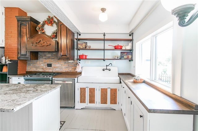 kitchen featuring open shelves, decorative backsplash, appliances with stainless steel finishes, a sink, and light wood-type flooring