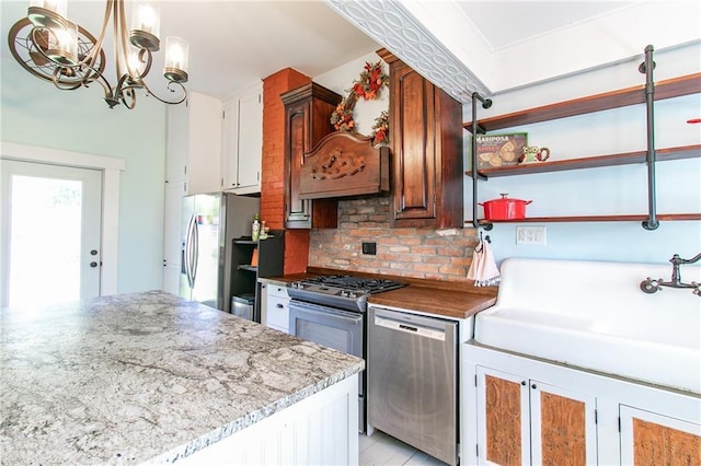 kitchen with a notable chandelier, open shelves, tasteful backsplash, appliances with stainless steel finishes, and a sink